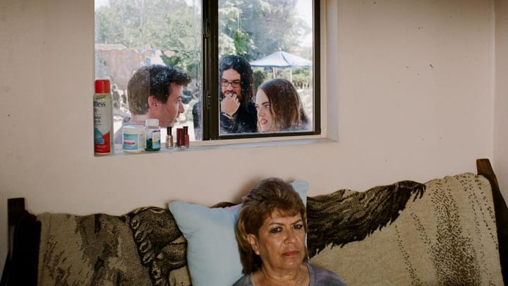 A woman on a couch; three people seen talking through a window.